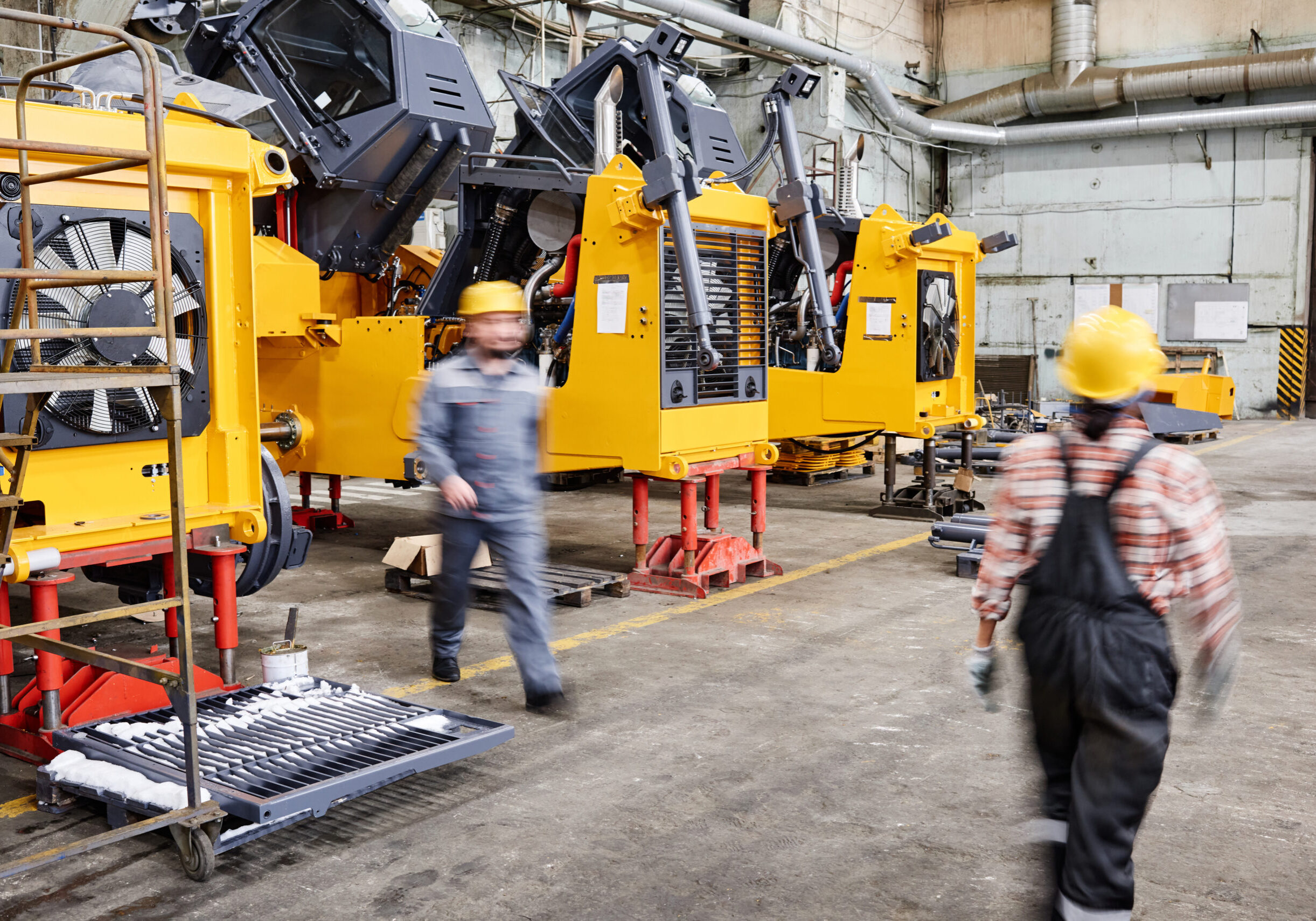 Blurred motion of two workers of industrial plant walking along spacious workshop with rows of huge machines and other equipment