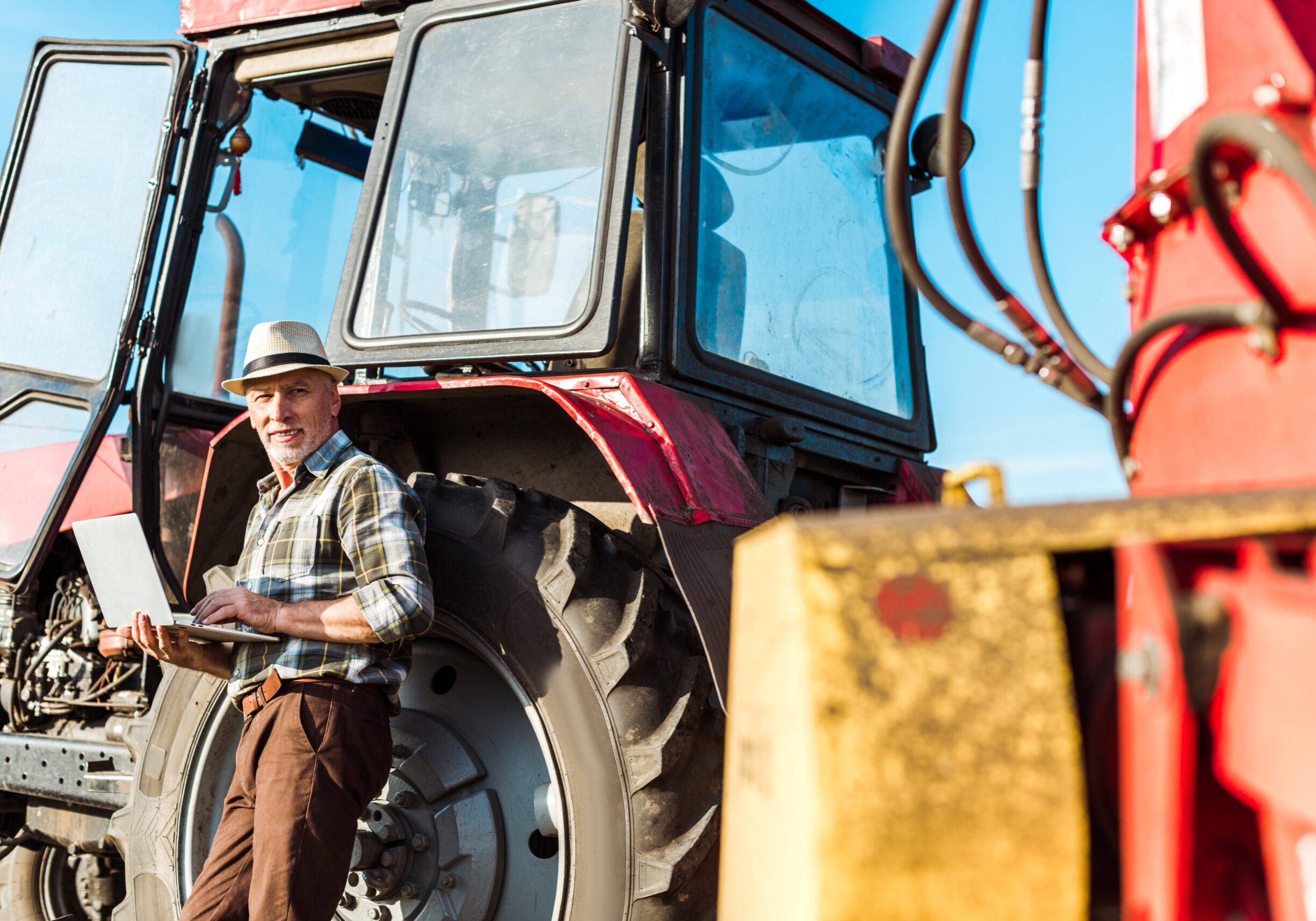 selective focus of happy farmer in straw hat using laptop near tractor