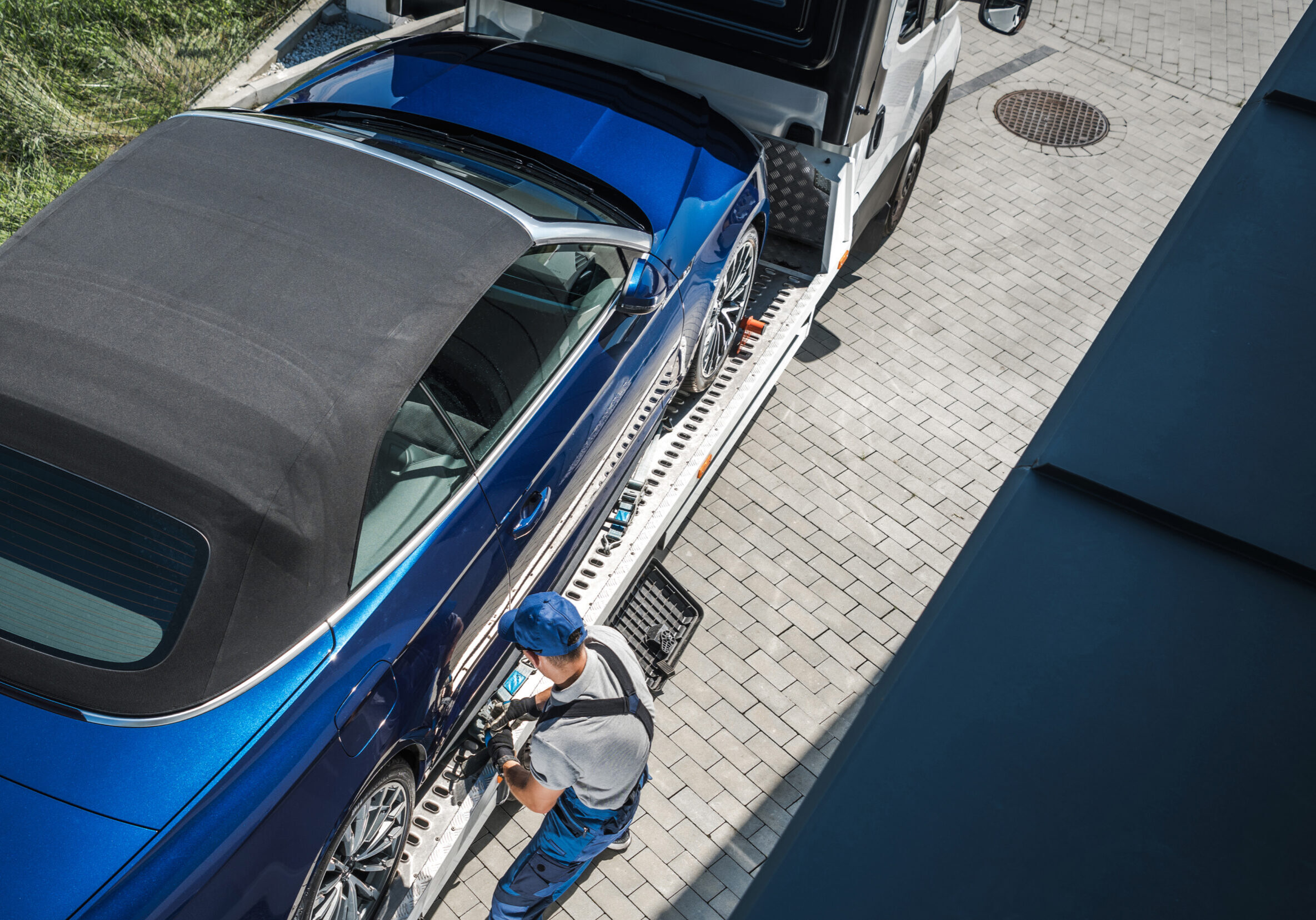 Automotive Industry Sales Theme. New Vehicle Home Delivery on a Towing Truck. Caucasian Driver Removing Safety Belts to Release the Car.